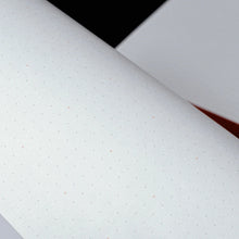 Load image into Gallery viewer, Close-up of a notebook with dotted pages on a black background
