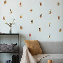 Load image into Gallery viewer, Wall with decorative beer mug decals, gray sofa, and small table with a vase.
